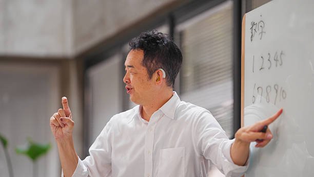 A deaf businessman is using a whiteboard and teaching sign language to his colleagues in a modern office.