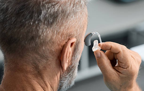 Senior man putting a hearing aid on his ear while visit his doctor at hearing clinic. Hearing solutions for elderly deafness people